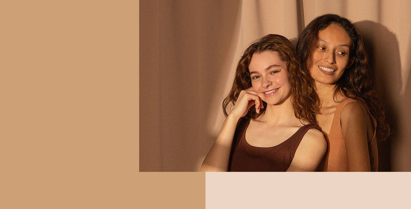 2 young women with a naturally colored backdorop smiling 